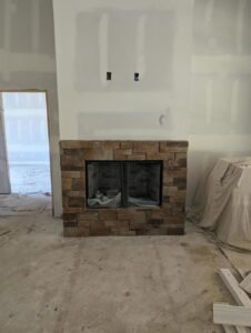 Stone fireplace with a black metal frame in a room under construction