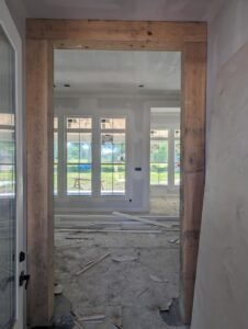 Home interior under construction, showing a doorway with a rustic wood beam and a built-in shelving unit.