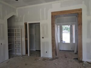 Home interior under construction, showing a doorway with a rustic wood beam and a built-in shelving unit.