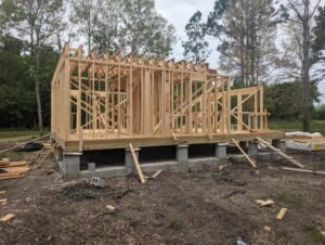 Construction progress on a house, featuring a pier and beam foundation and exposed wooden framing.