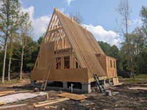 Construction progress on a modern A-frame home, showcasing the exposed wooden frame and roofline.