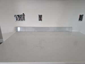 White countertop with marble-like veining, partially installed backsplash tiles, and visible electrical outlets in an unfinished kitchen space.